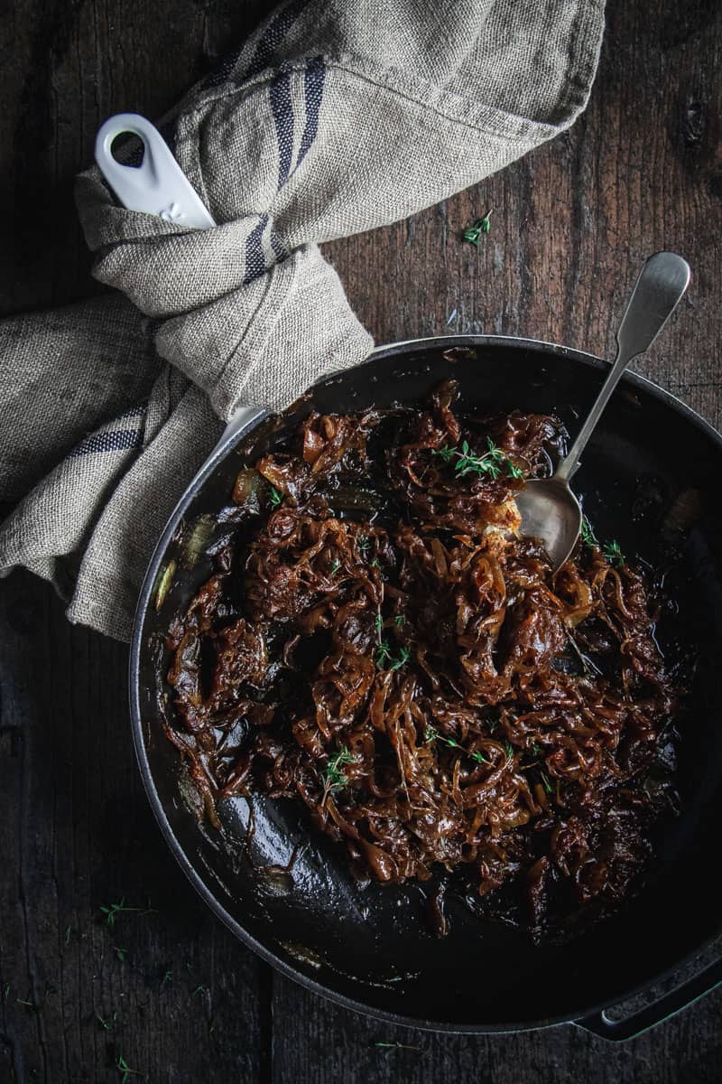 A cast iron skillet full of slow cooked caramelized balsamic onion jam scattered with fresh thyme.