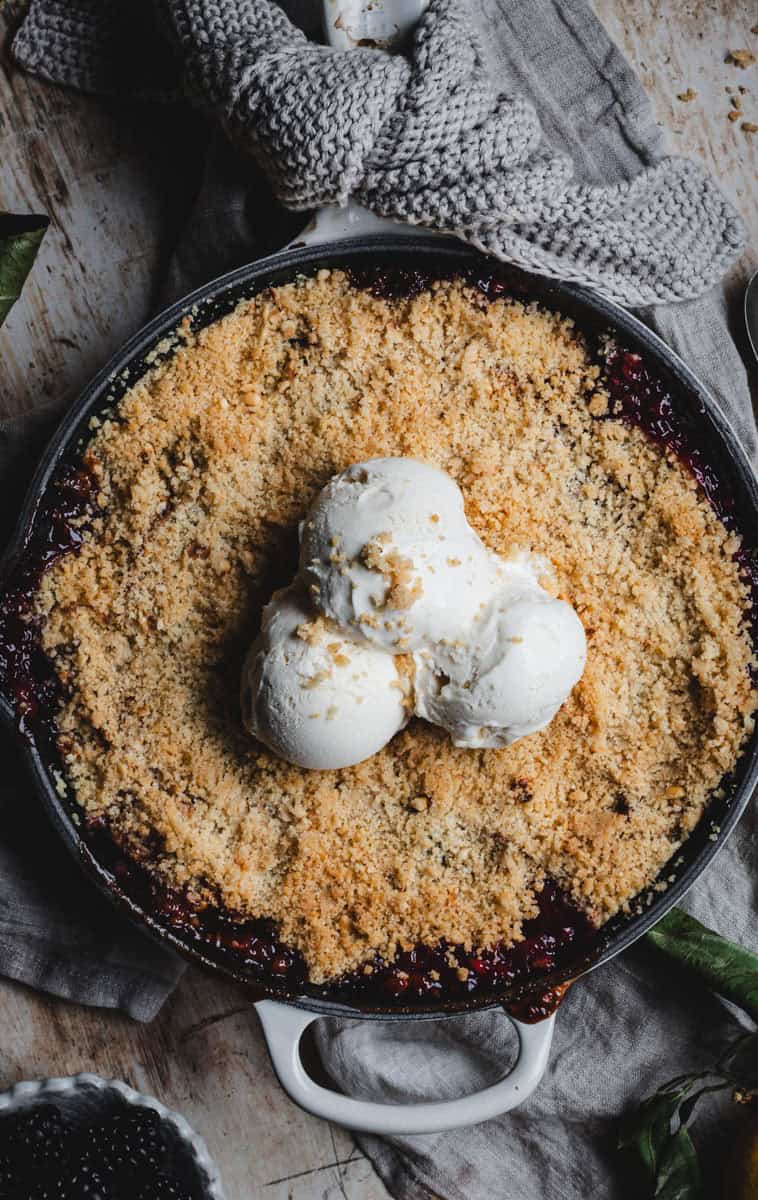 An apple and blackberry crumble topped with ice cream in a skillet.