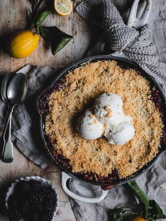 The baked apple and blackberry crumble in a cast iron skillet topped with scoops of vanilla ice cream.