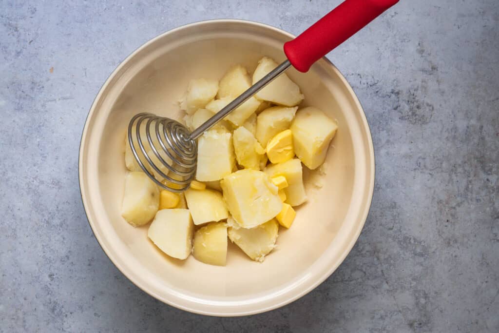 Cooked potatoes being mashed in a little batter and milk.