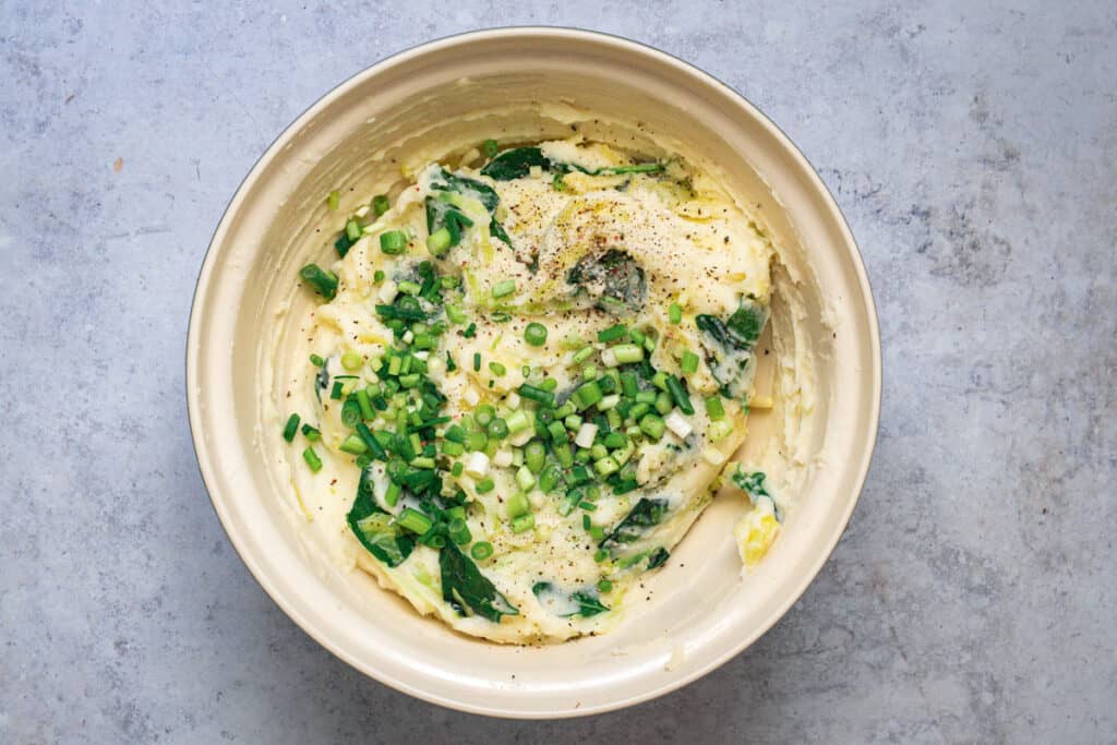 Spring onions are added to the bowl and the colcannon is seasoned with salt and pepper.