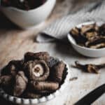 The finished dehydrated mushrooms. in small bowls on a wooden bench. A small wooden handled knife sits beside.