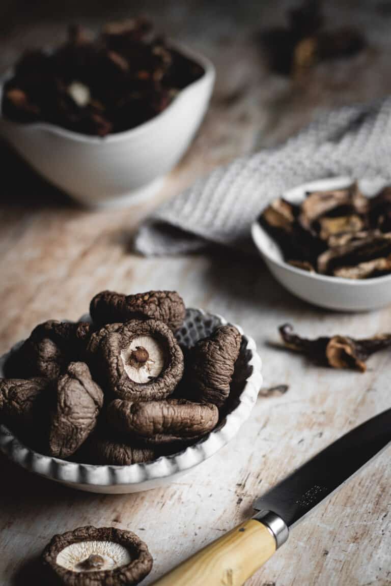 The finished dehydrated mushrooms. in small bowls on a wooden bench. A small wooden handled knife sits beside.