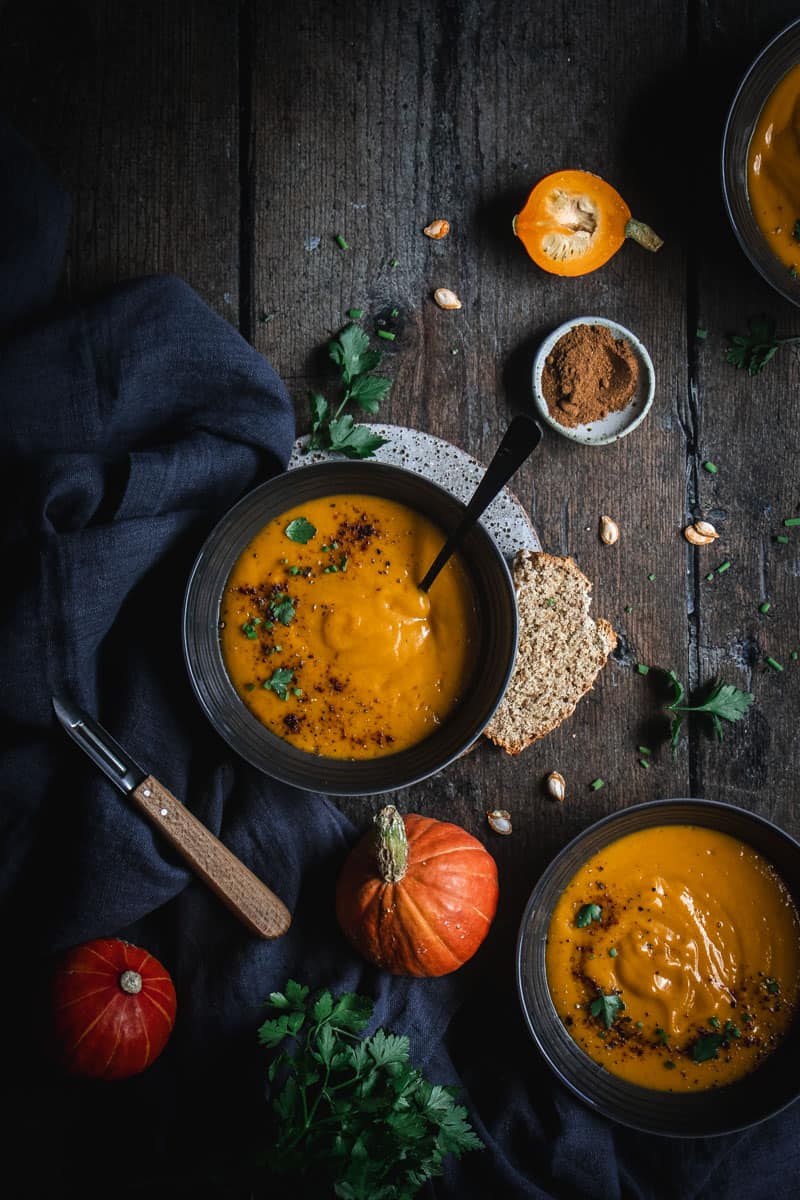 two bowls of roast butternut chipotle soup without cream on a timber bench.