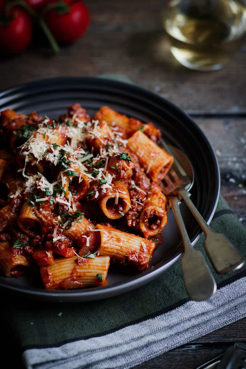 Close up of a bowl of rigatoni bolognese with cutlery in the bowl.