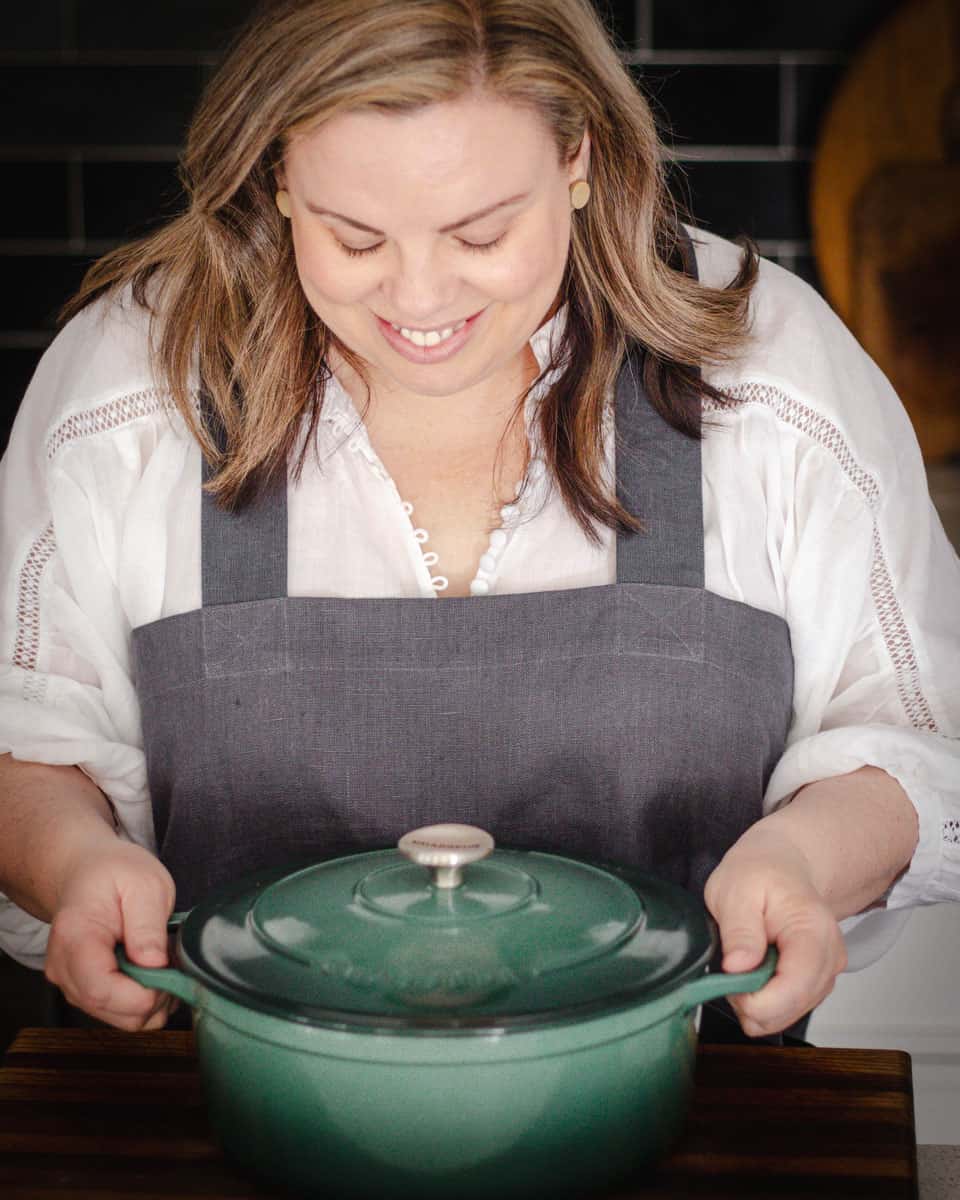 Emma holding a green Dutch oven and looking down at it.