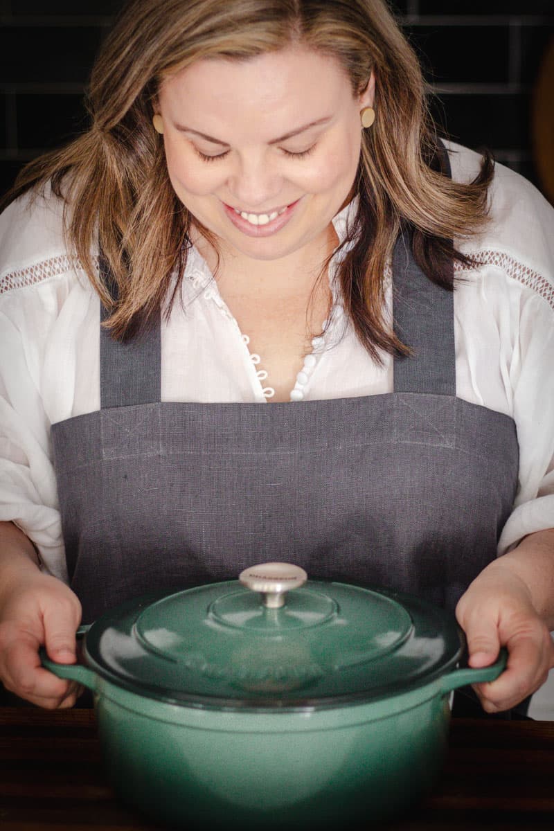 Emma Lee holding a green dutch oven and looking down at it.