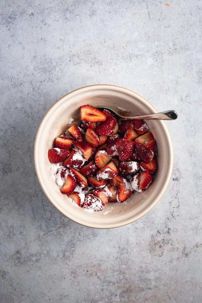 Strawberries being coated in balsamic vinegar and icing sugar.