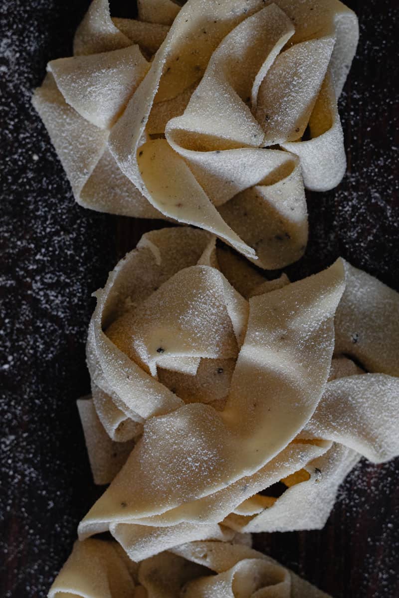 A close up of handmade fettuccine nests drying on a board dusted with semolina.