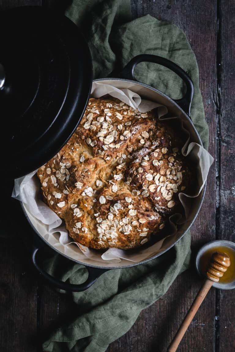 A black cast iron Dutch oven with a loaf of soda bread in it and a pot of honey beside.