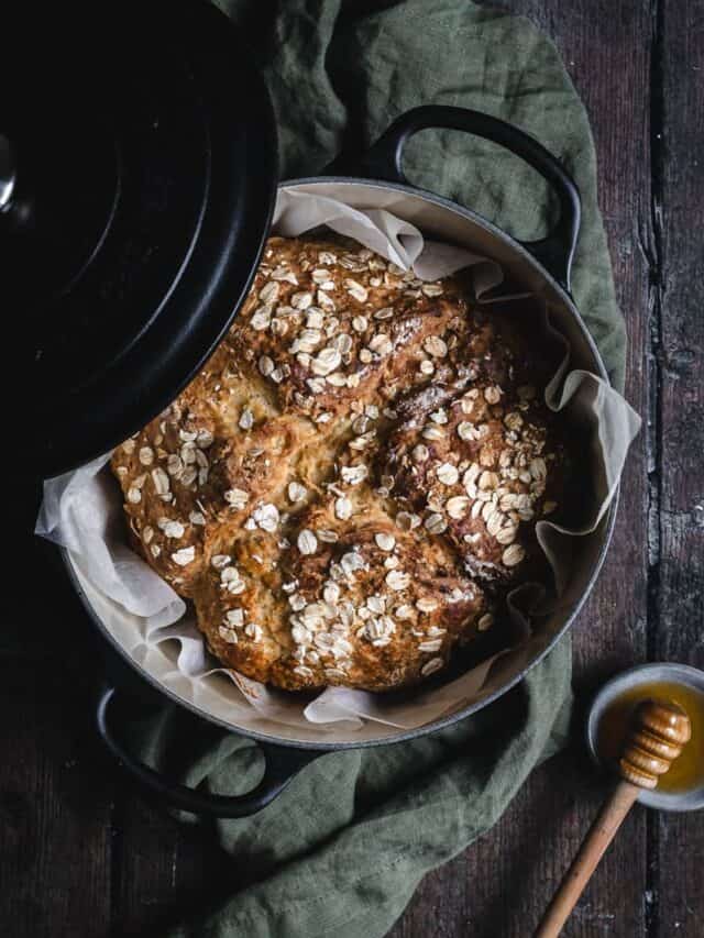 A black cast iron Dutch oven with a loaf of soda bread in it and a pot of honey beside.