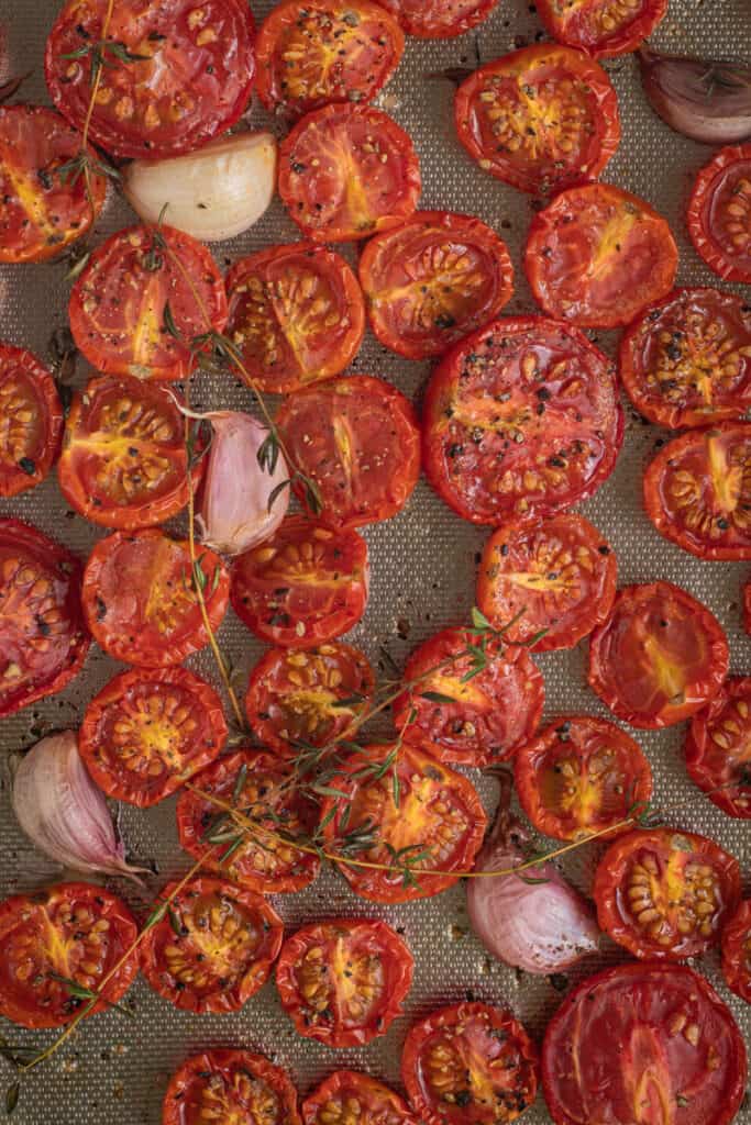 A close up of oven roasted cherry tomatoes in a roasting pan with thyme scatted on top.
