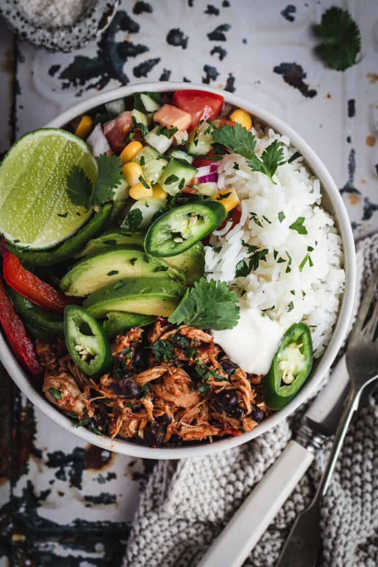 A chipotle chicken salad and rice bowl is on a vintage cream and green tray. A pot of salt and cutlery sit beside.