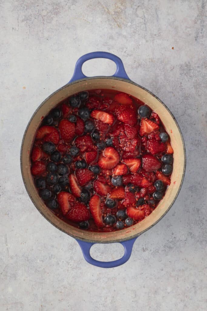 Berries macerating in lemon juice and sugar in a blue cast iron Dutch oven.
