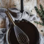 A copper frying pan full of roast lamb gravy. A whisk sits inside the frying pan and fresh rosemary if beside the pan.