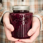 A boy holding a jar of three berry jam with both hands.