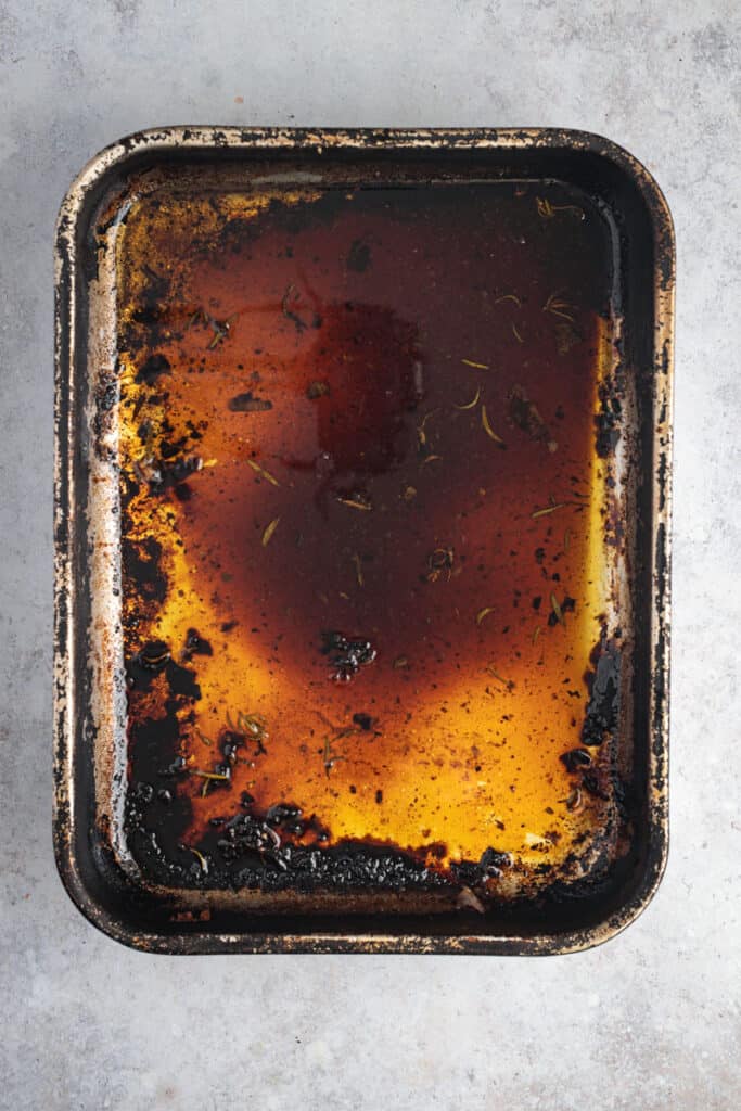 A stainless steel roasting pan with roast lamb pan drippings in the base of it.