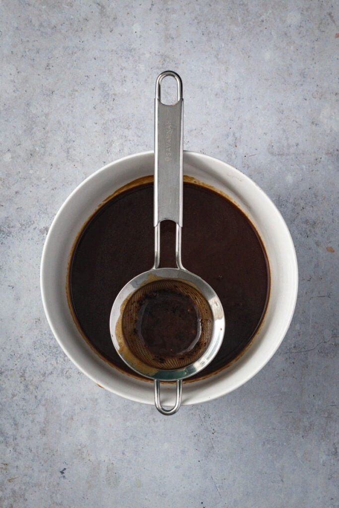 A white bowl with a metal strainer straining the gravy.