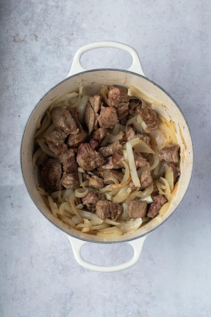 Browned chunks of beef  and sauteed onion mixed together in the pot.