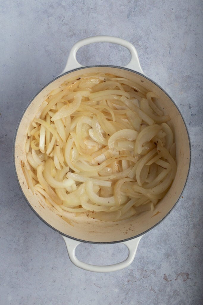 A cream enamel cast iron pot of onions being sauteed with olive oil.