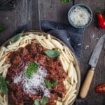 flatlay of a frypan of slow cooked beef and red wine ragu on a bed of capunti pasta, with parmasean and basil leaves.