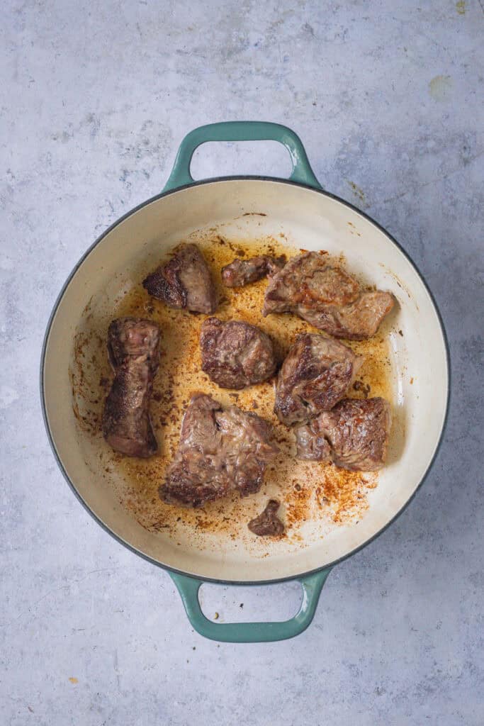 Beef chunks browning in oil in a green cast iron pot.
