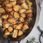 An oval pan of oven roasted rosemary and garlic potatoes. Fresh rosemary and garden scissors sit beside the pan.