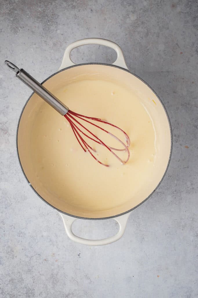 The sauce is thickening and becoming smooth from whisking with the red whisk.