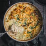 A black Le Creuset cast iron Dutch oven with a fish pie in it. A serving has been scooped out revealing the creamy seafood mornay inside.