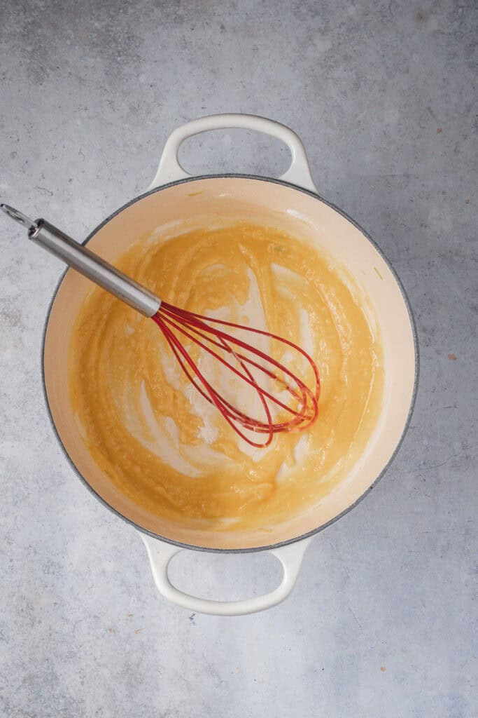 A red whisk is stirring the butter and flour together to form a roux.