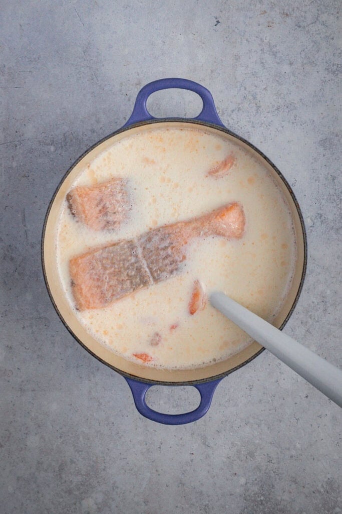 Seafood poaching in milk in a blue Dutch oven.
