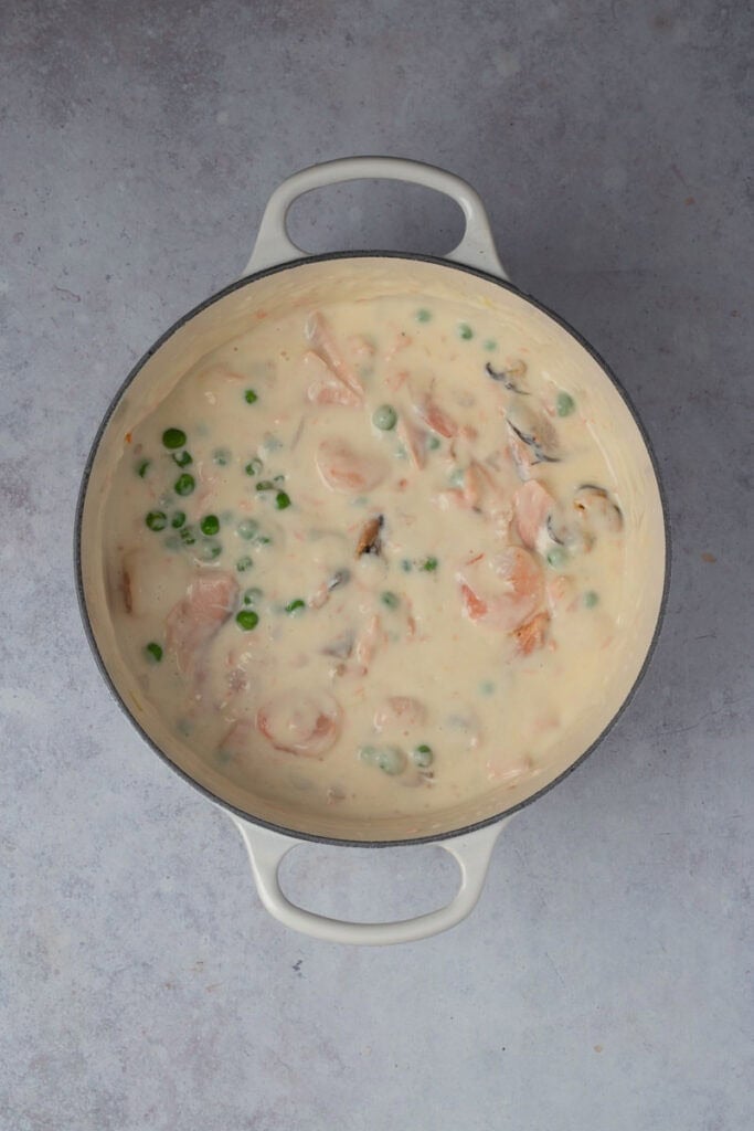 The creamy sauce with the seafood, peas and herbs added to the pot and combined.