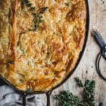 A close up of a Chicken bacon a leek pot pie with a puff pasty top in an oval copper dish. Small black kitchen scissors and a few sprigs of fresh thyme sit beside.