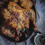 A roasted herb chicken with roasted vegetables in an oval copper pan.