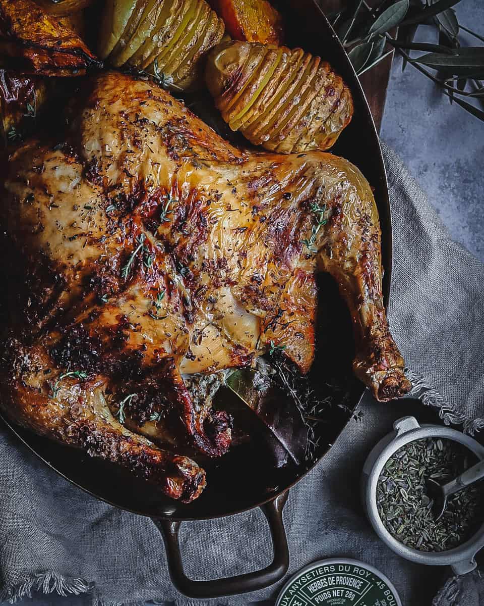 A roasted herb chicken with roasted vegetables in an oval copper pan.