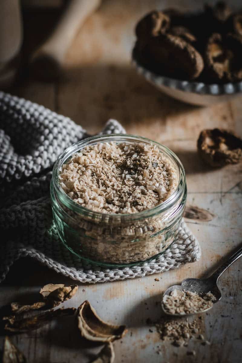 A small jar sits under a checkered cloth, the jar is holding some light brown salt.