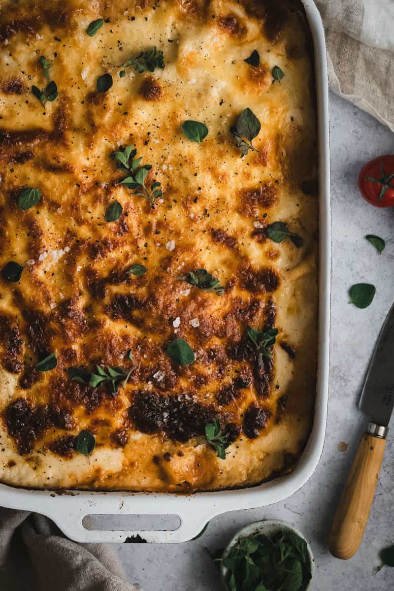 Close up of the lasagna with a small knife to the right and a tomato beside.