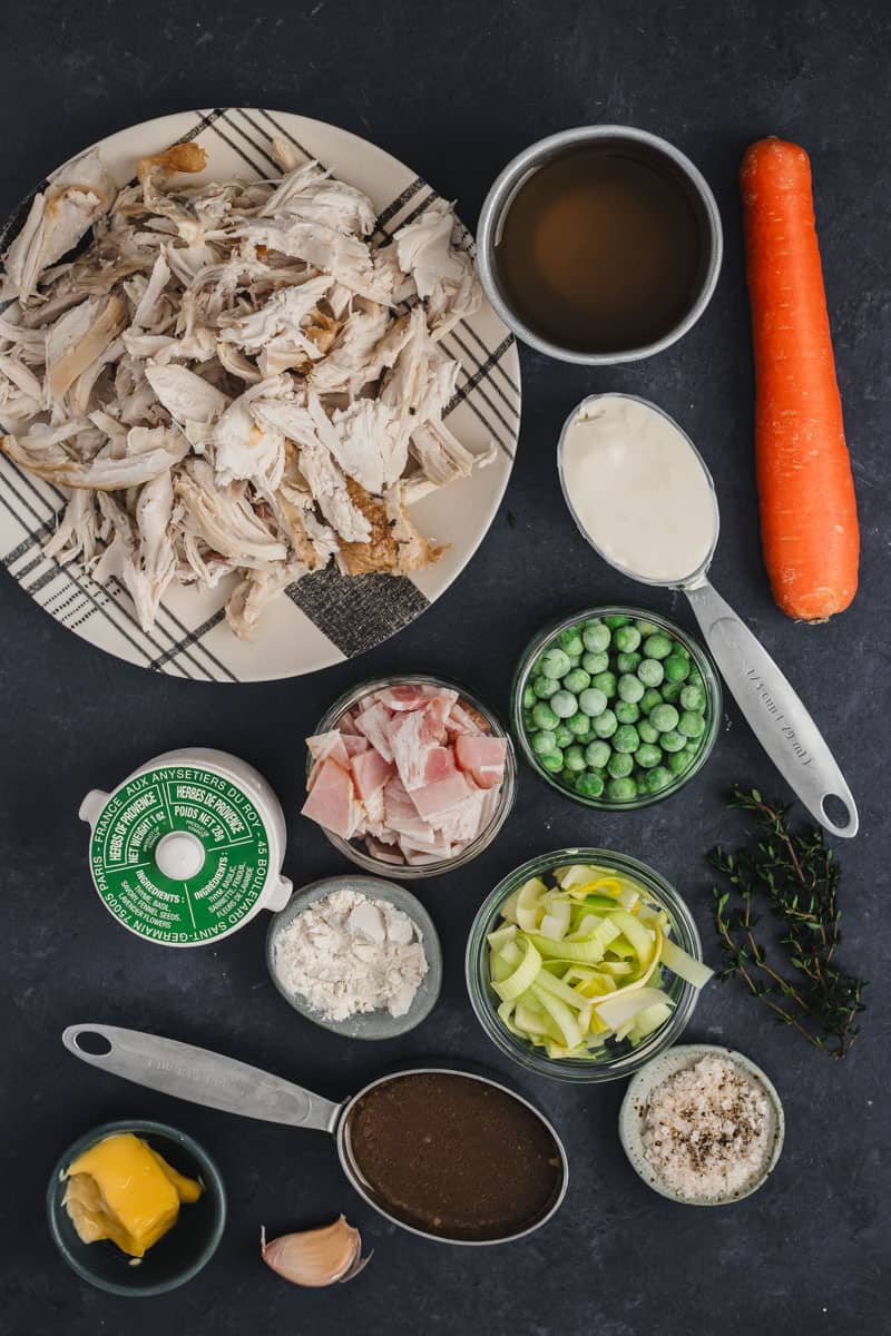 All the ingredients you need to make a chicken, bacon and leek pot pie on a navy blue background.