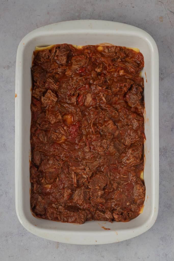 The completed ragu layer has covered the pasta sheet layer in the roasting pan.