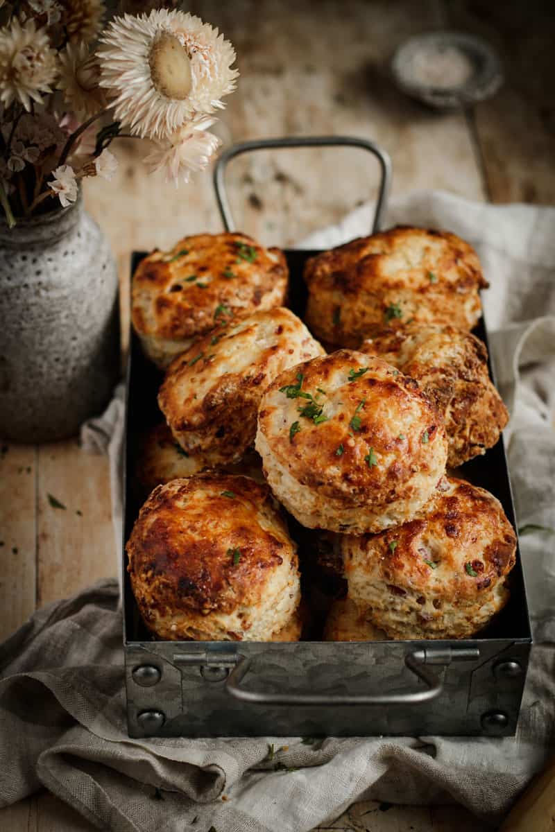 A metal tray of cheese and bacon scones. A small bunch a dried flowers sit beside.