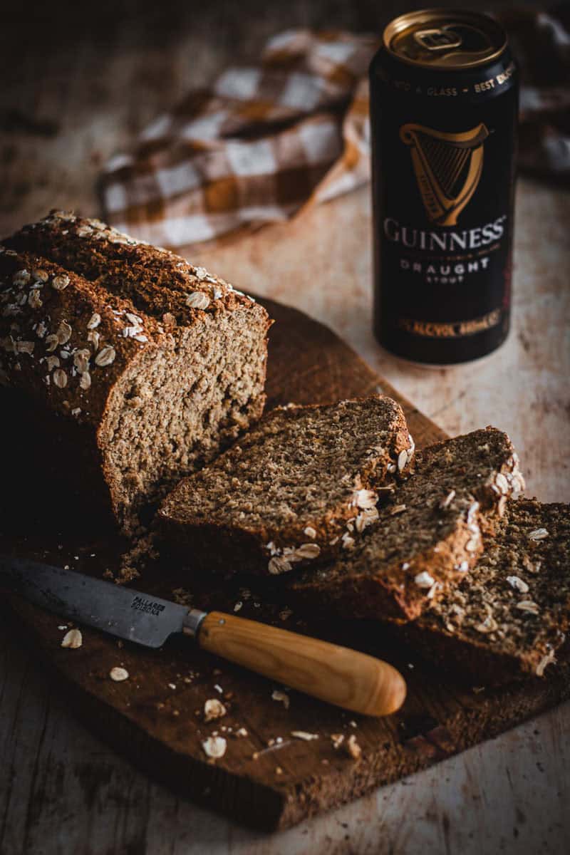 A loaf of Guinness sliced with a small knife beside it. A can of Guinness beer sits behind. 