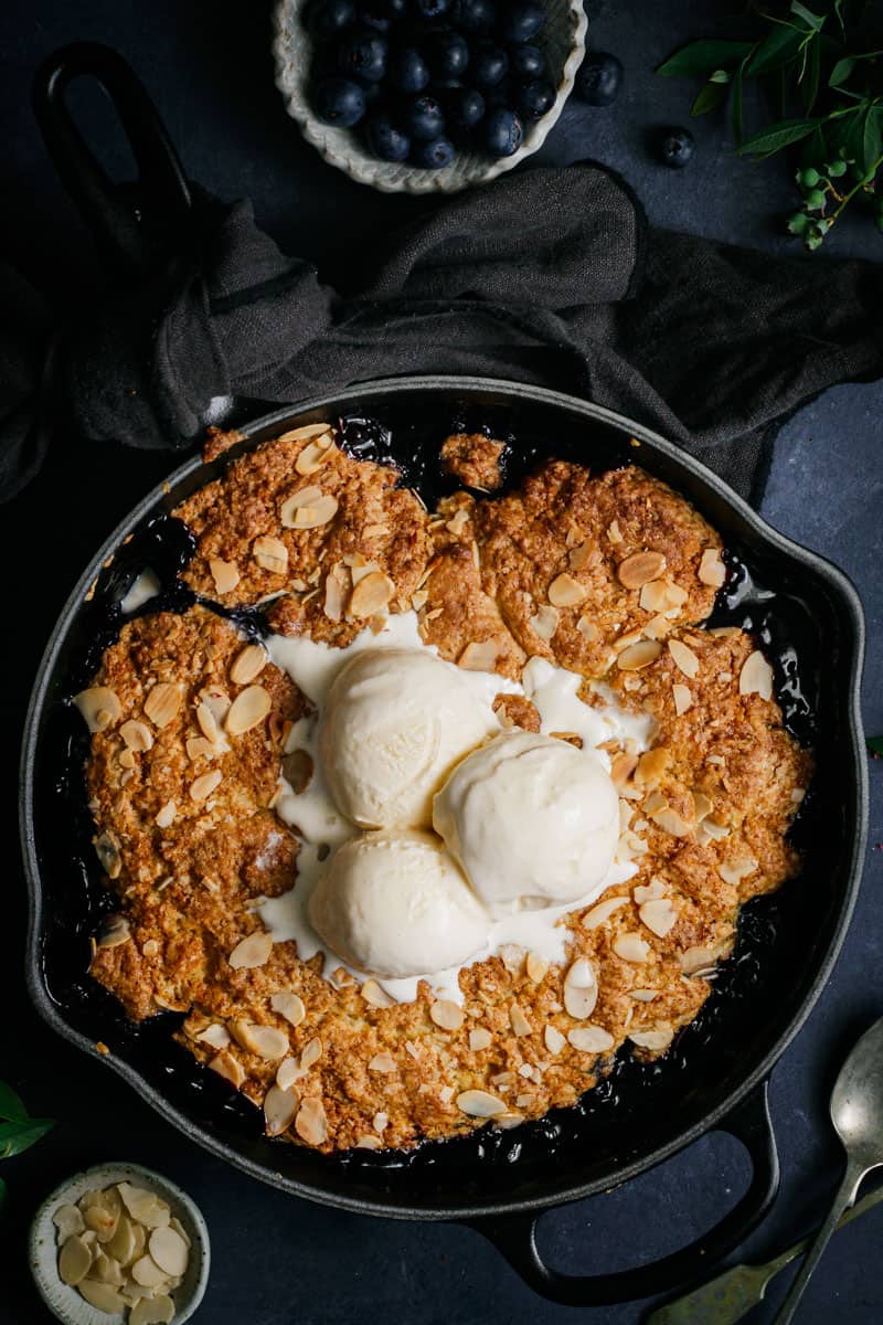 A skillet blueberry cobbler with three scoops of vanilla ice cream in the center.