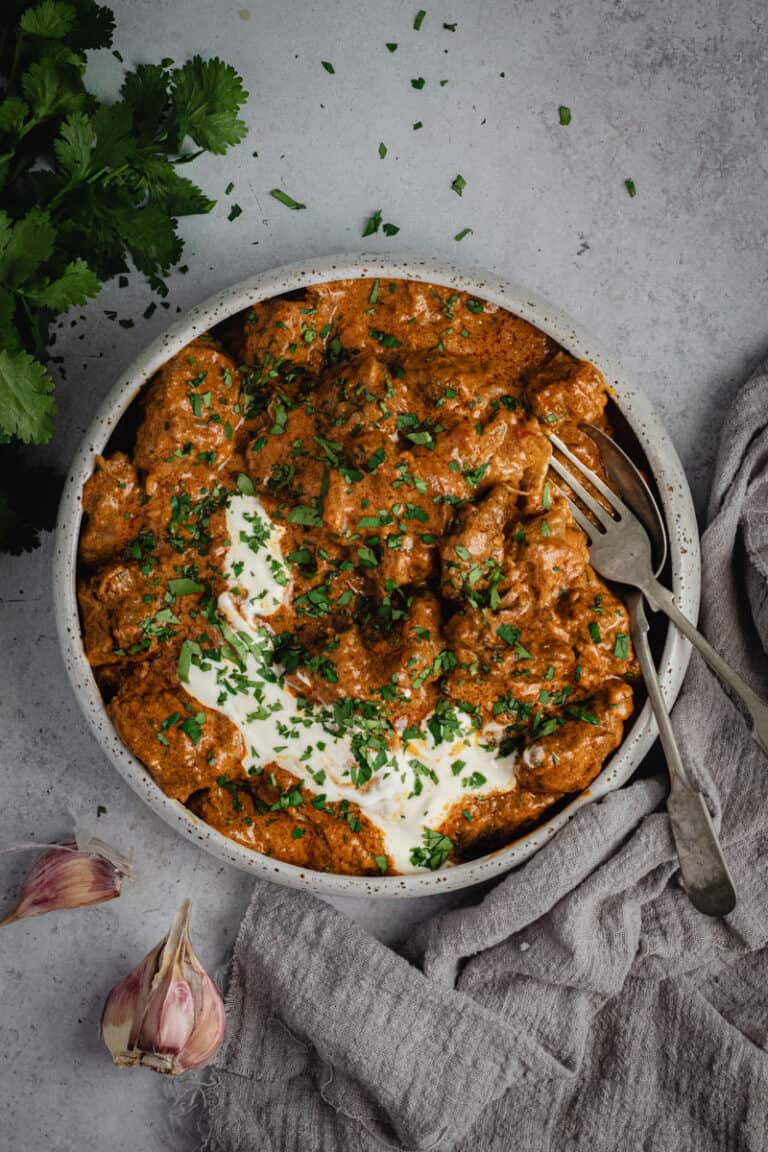 A bowl of slow cooked beef curry on a bowl. It's garnished with Greek yogurt and freshly chopped coriander.
