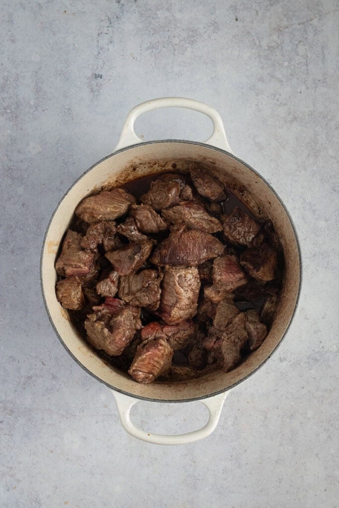 Browned chunks of beef in a cream enamel cast iron Dutch oven.