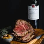 A rare medium rare roast beef being carved on a timber board. A bottle of Angullong red wine sits behind.