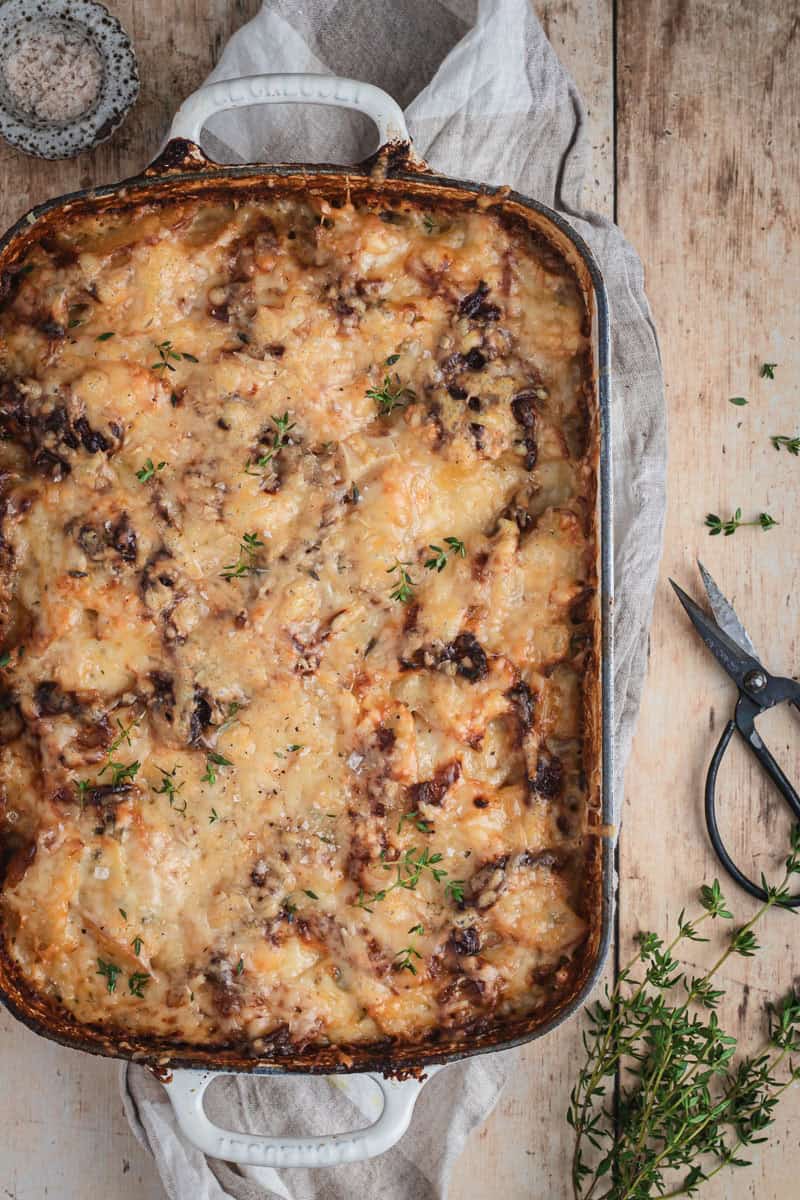 A just out of the oven pan full of potato bake and caramelized onions. A small pair of herb scissors sit beside with some fresh thyme.