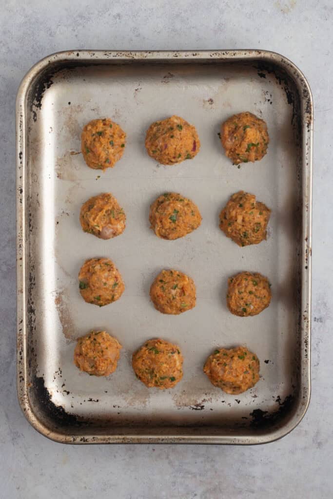 Rolled chicken meatballs on a baking tray ready for the oven.