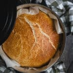 A black Dutch oven with a loaf of homemade bread in it.