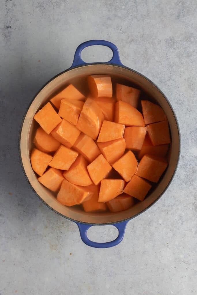 A blue cast iron pot filled with cubes of sweet potato and water.