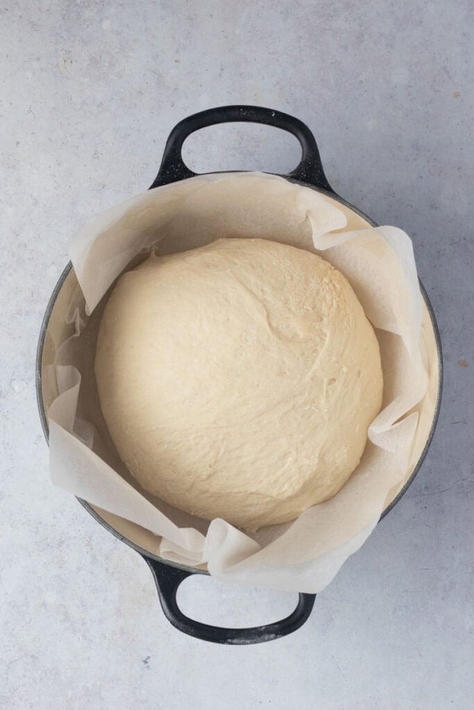 The loaf has been shaped and put on baking paper sitting in a black Dutch oven.